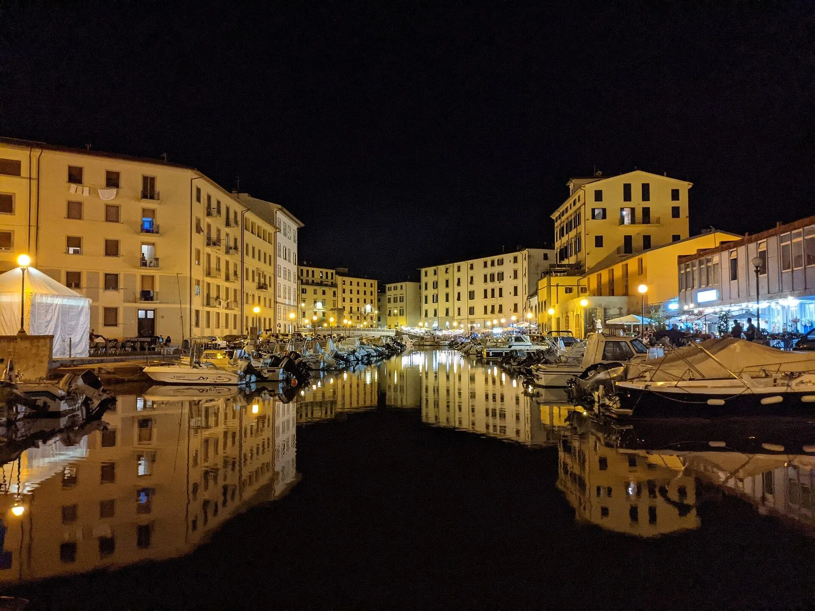 Un canale dei fossi medicei di Livorno di notte, tra gli Scali delle Barchette e gli Scali delle Ancore, con barche ormeggiate e i palazzi illuminati che si riflettono nell’acqua