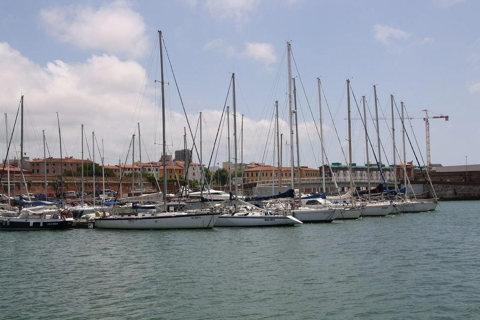Barche a vela ormeggiate nel Porto Mediceo di Livorno, con le mura di mattoni e gli edifici del porto sullo sfondo sotto un cielo con nuvole