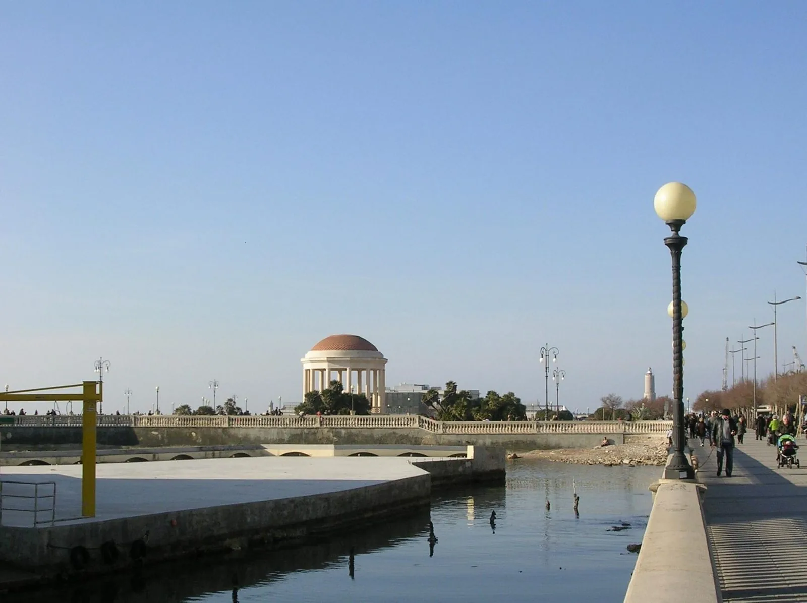 Il lungomare di viale Italia a Livorno con i lampioni a globo, persone a passeggio e, in lontananza oltre lo specchio d'acqua, un gazebo con la cupola rossa